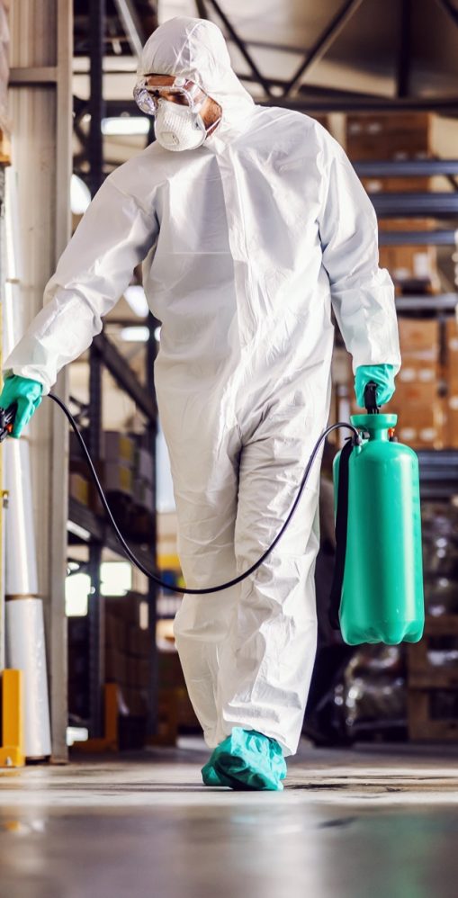 Man in protective suit and mask disinfecting warehouse full of food products from corona virus / covid-19.